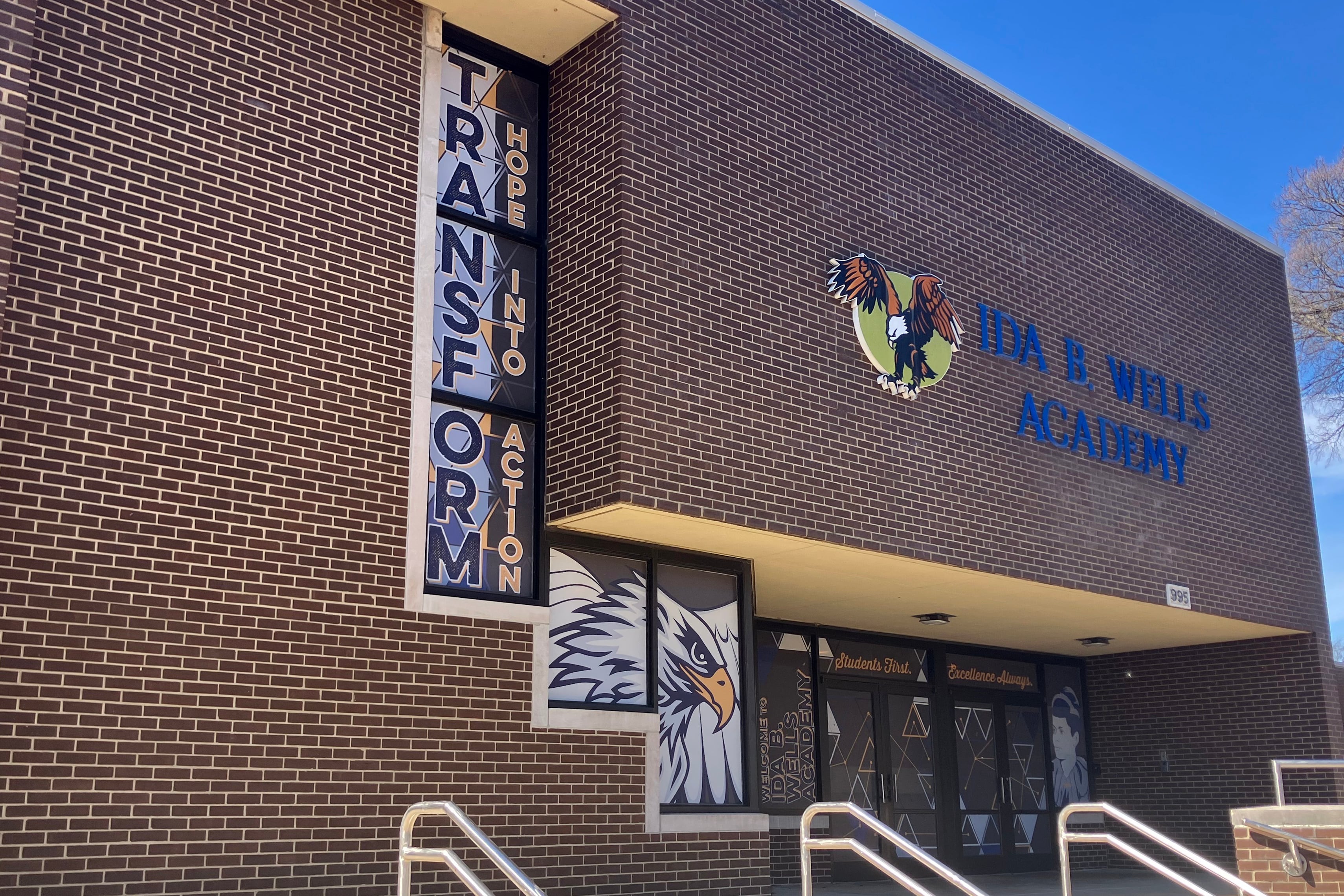 A photograph of the outside of a brick school building with blue letters on the side.