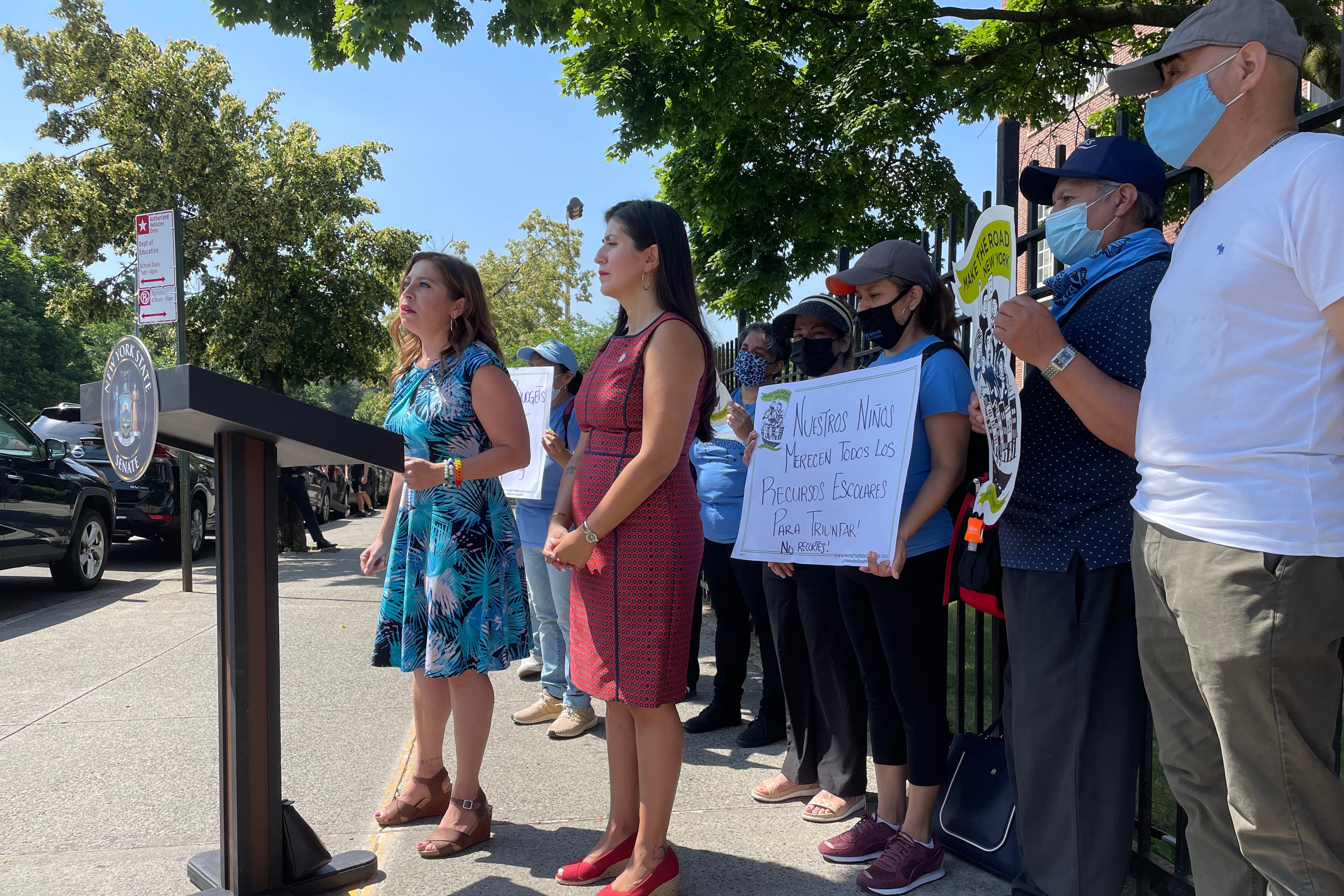 Two women stand behind a lectern in front of a school.