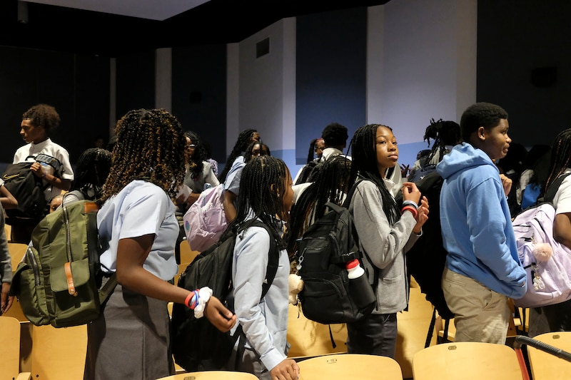 A photograph of a line of students carrying backpacks in a row in an auditorium.
