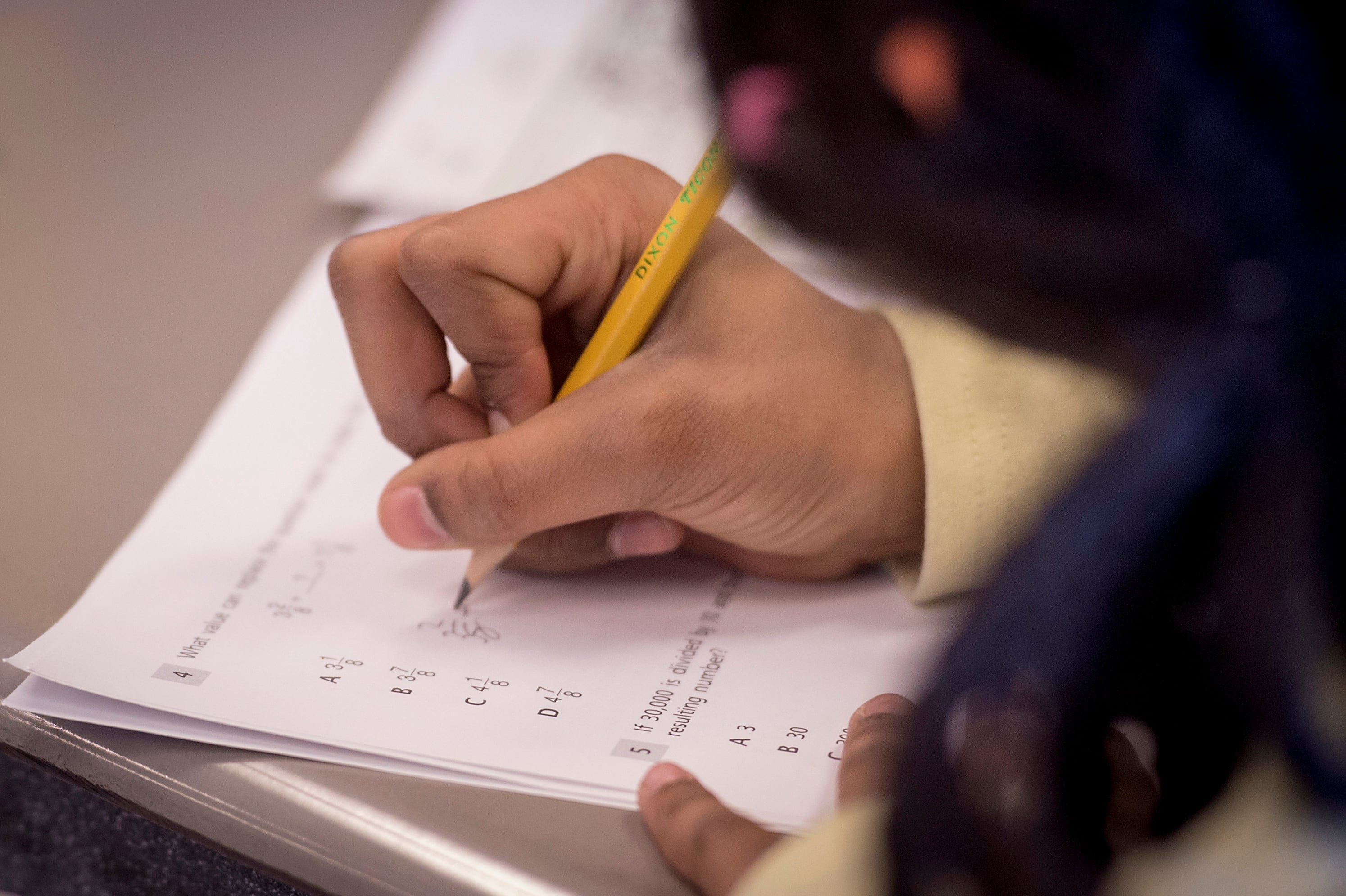 A person's hand is holding a pencil and working on a worksheet.