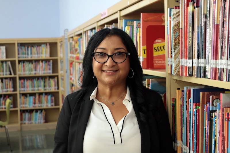 A photograph of a brown woman with dark hair and posing for a portrait in a library.