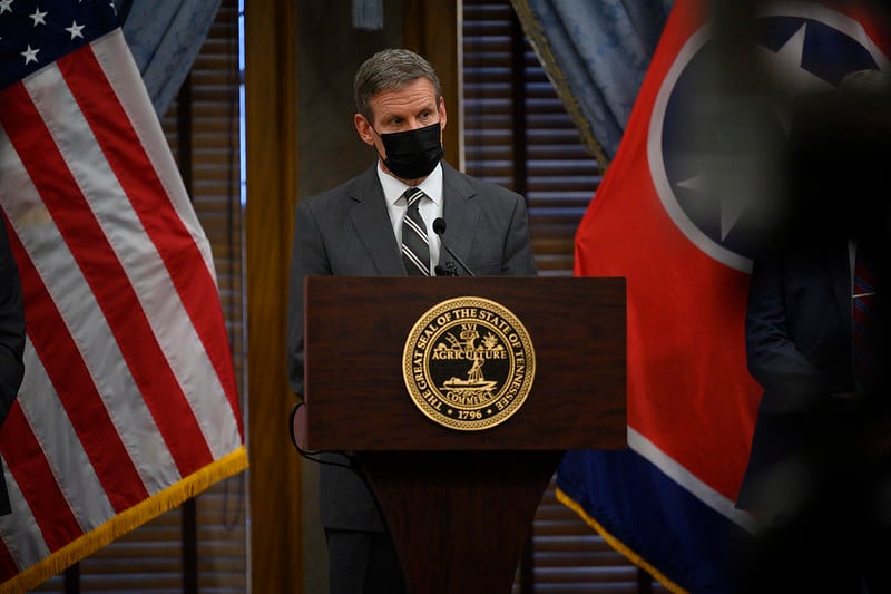 Tennessee Gov. Bill Lee stands alone and masked a podium with the U.S. flag to his left and the state flag to his right.