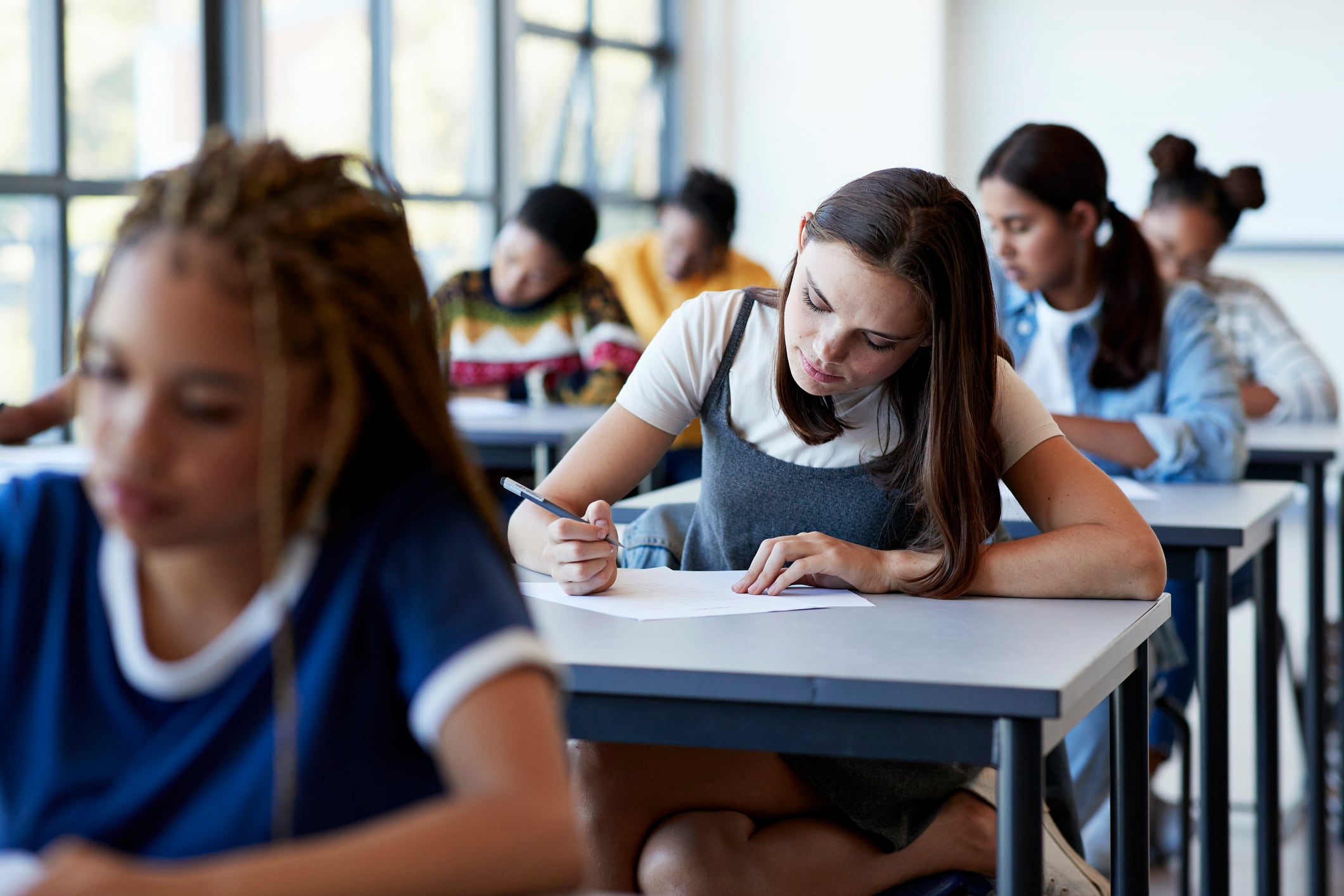 Students sit at white desks taking exams with paper and pencil