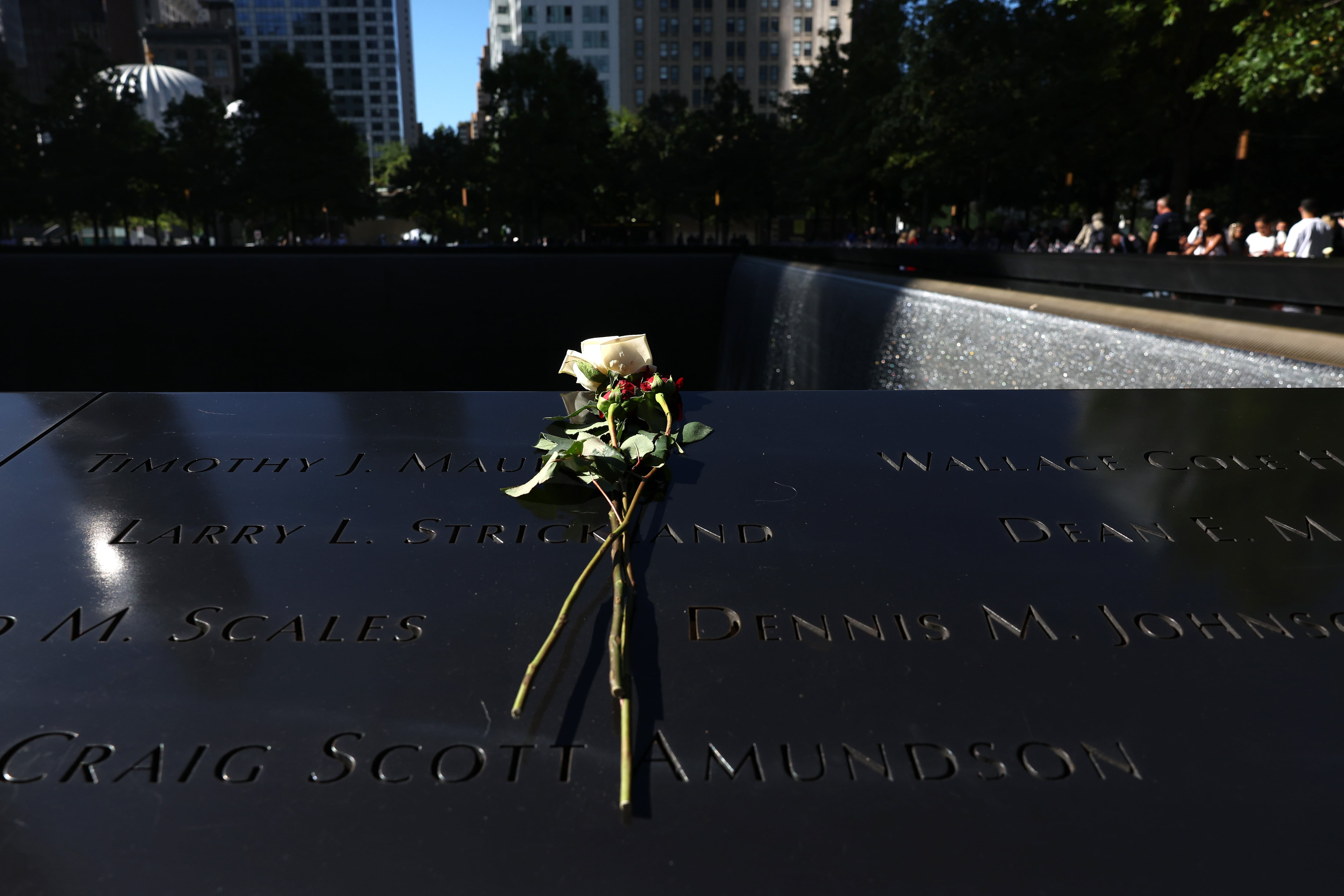 A flower is placed on a name on a black low wall.