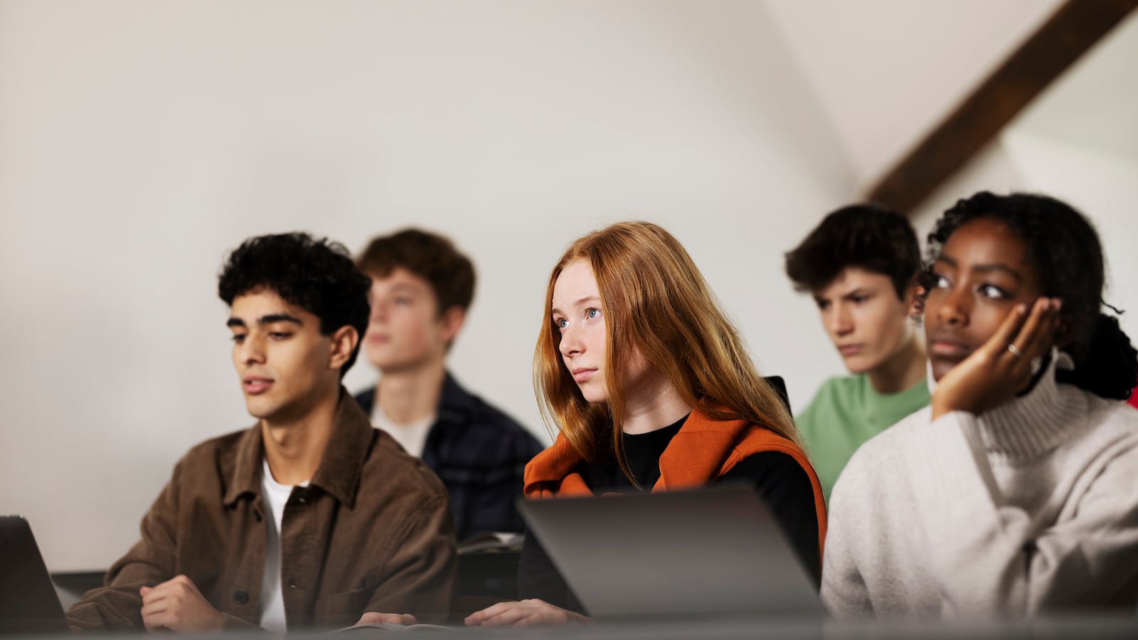Five students sit in a classroom with a white background.