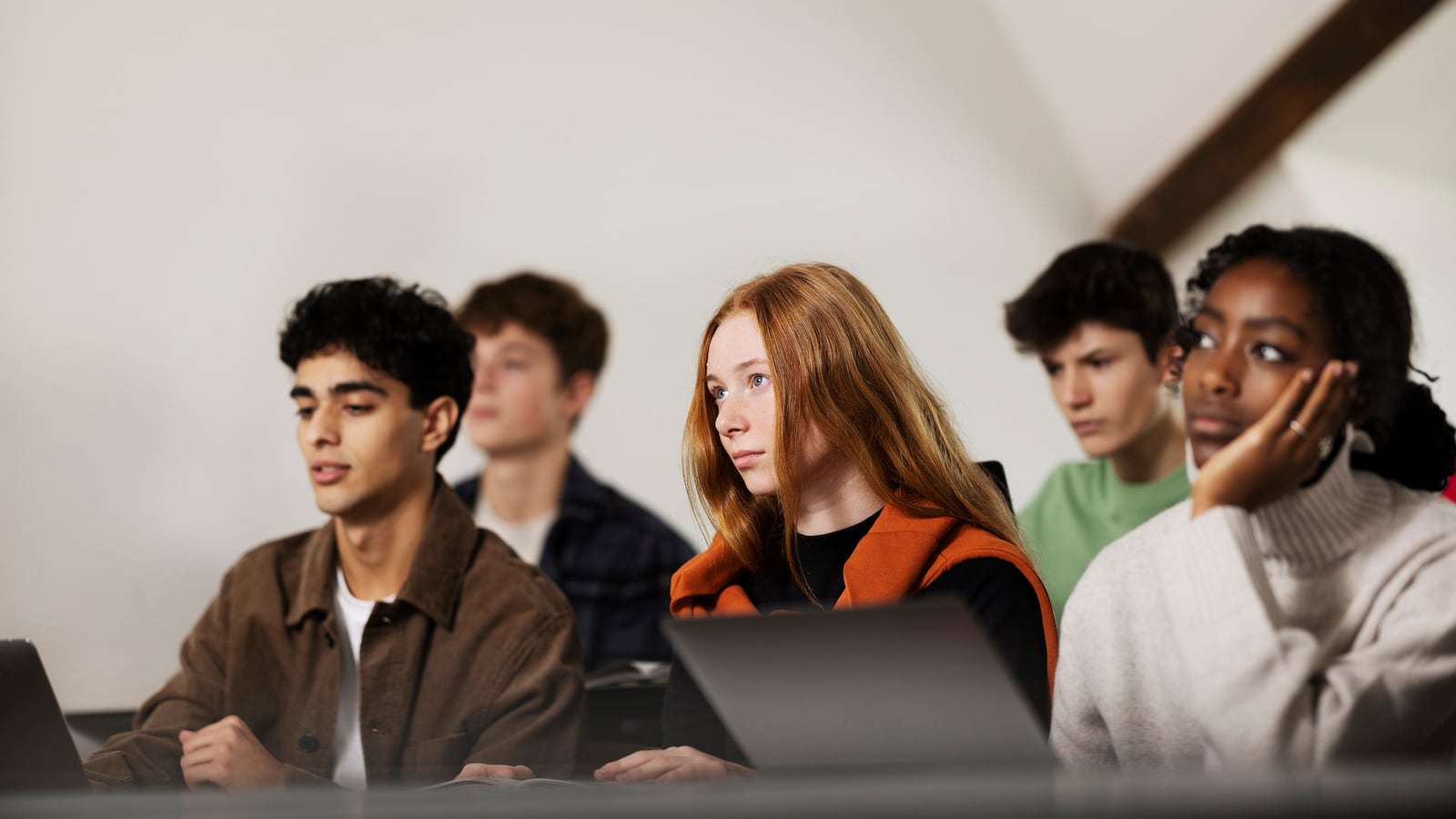 Five students sit in a classroom with a white background.
