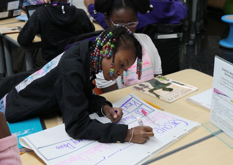 A girl in a dark top writes with a marker.