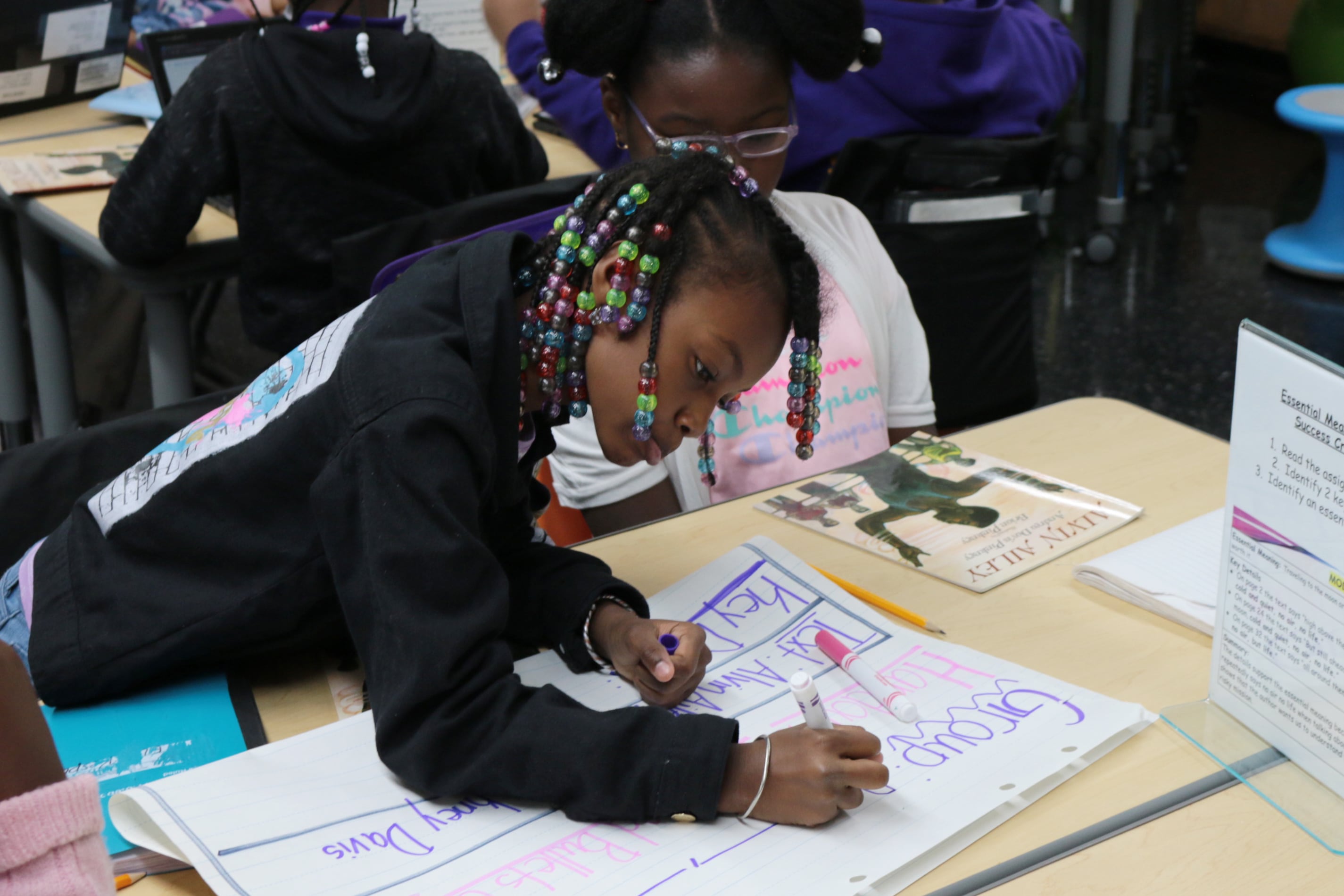 A girl in a dark top writes with a marker.