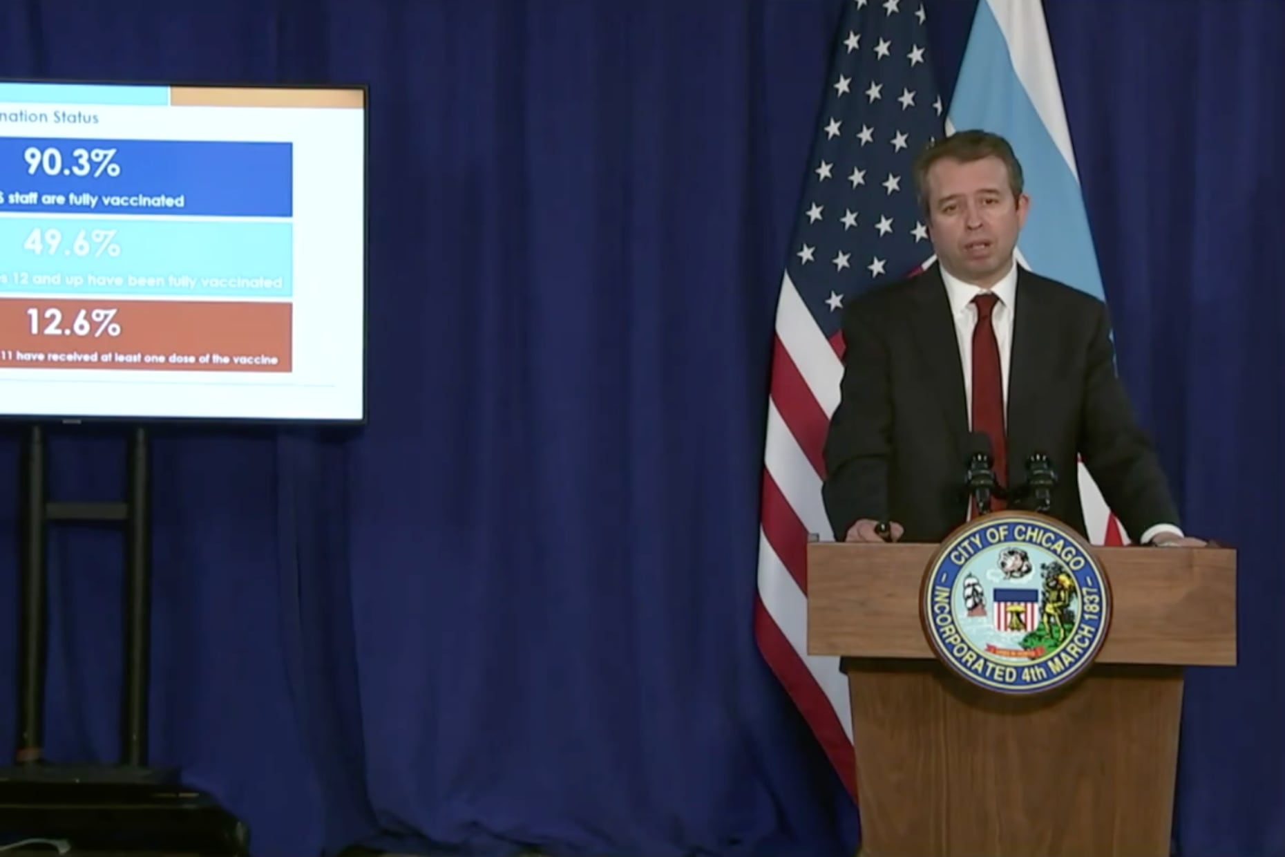 A man stands in a blue suit stands at a podium with the Chicago seal.