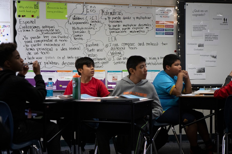 Students sit at a table in a classroom.