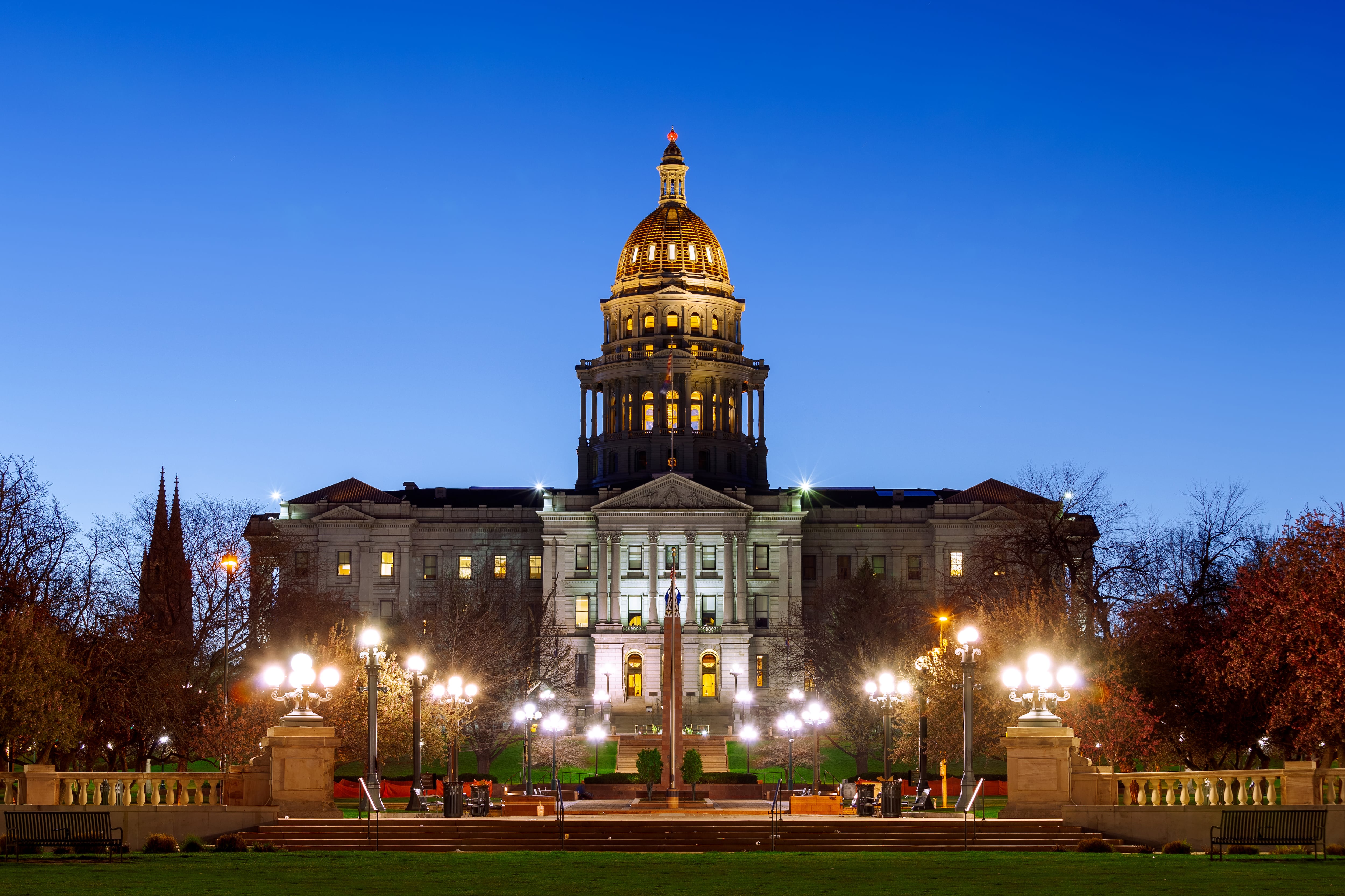 A view of the Colorado Capitol building from the front entrance with outdoor lights on and a dark blue sky in the background.