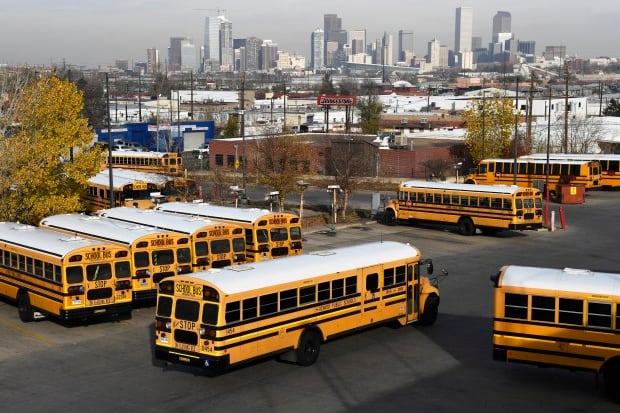 Yellow school buses head out past other parked buses in a terminal lot.