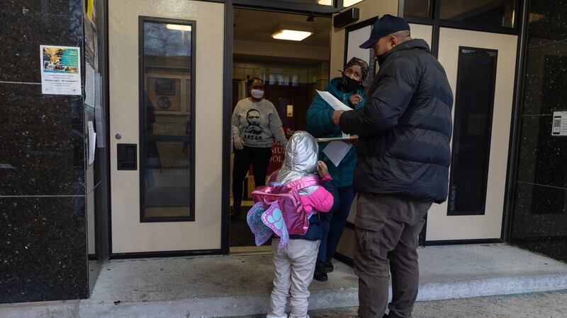 A father drops off his daughter at school. They are wearing winter clothing, and the girl is wearing a bright pink jacket and a butterfly backpack.