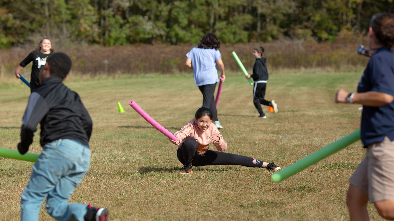 Fifth graders participate in a tag game using pool noodles to avoid contact.