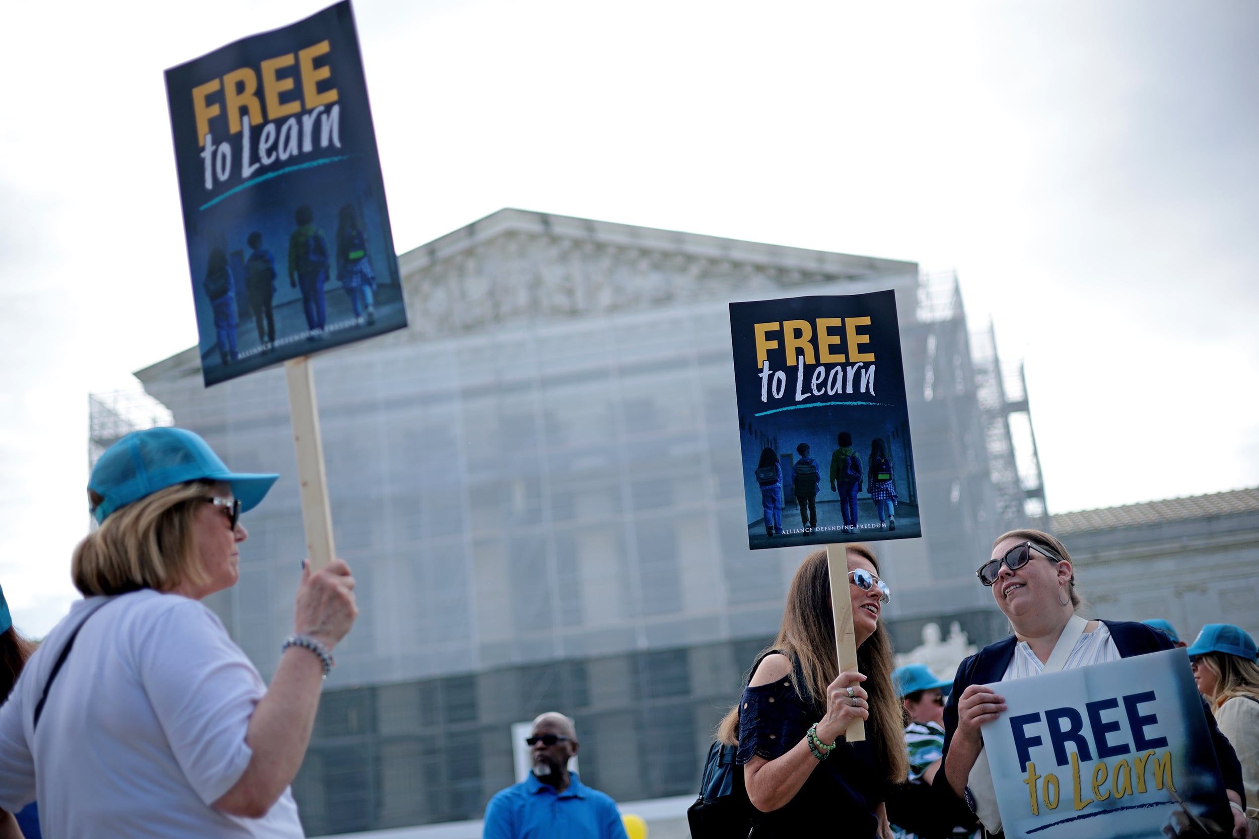 A photograph of a small group of white women holding up signs outside of the U.S. Supreme Court building with a cloudy sky.