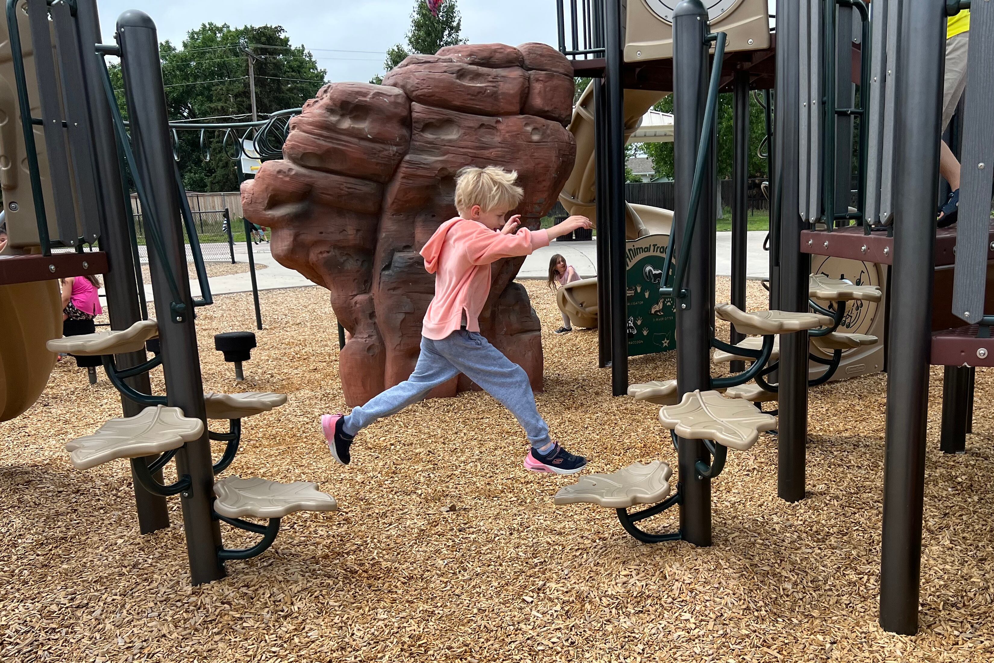 A third grade child in a peach-colored shirt leaps from one plastic toadstool to another on an outdoor school playground.