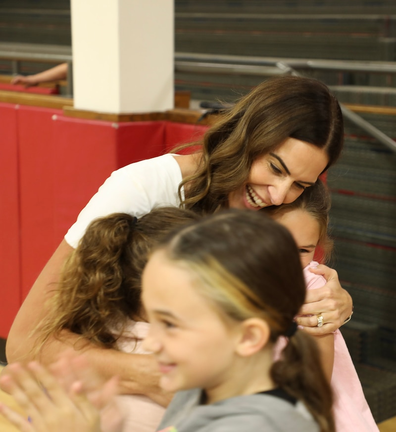 A photograph of a woman hugging young children during a celebration.