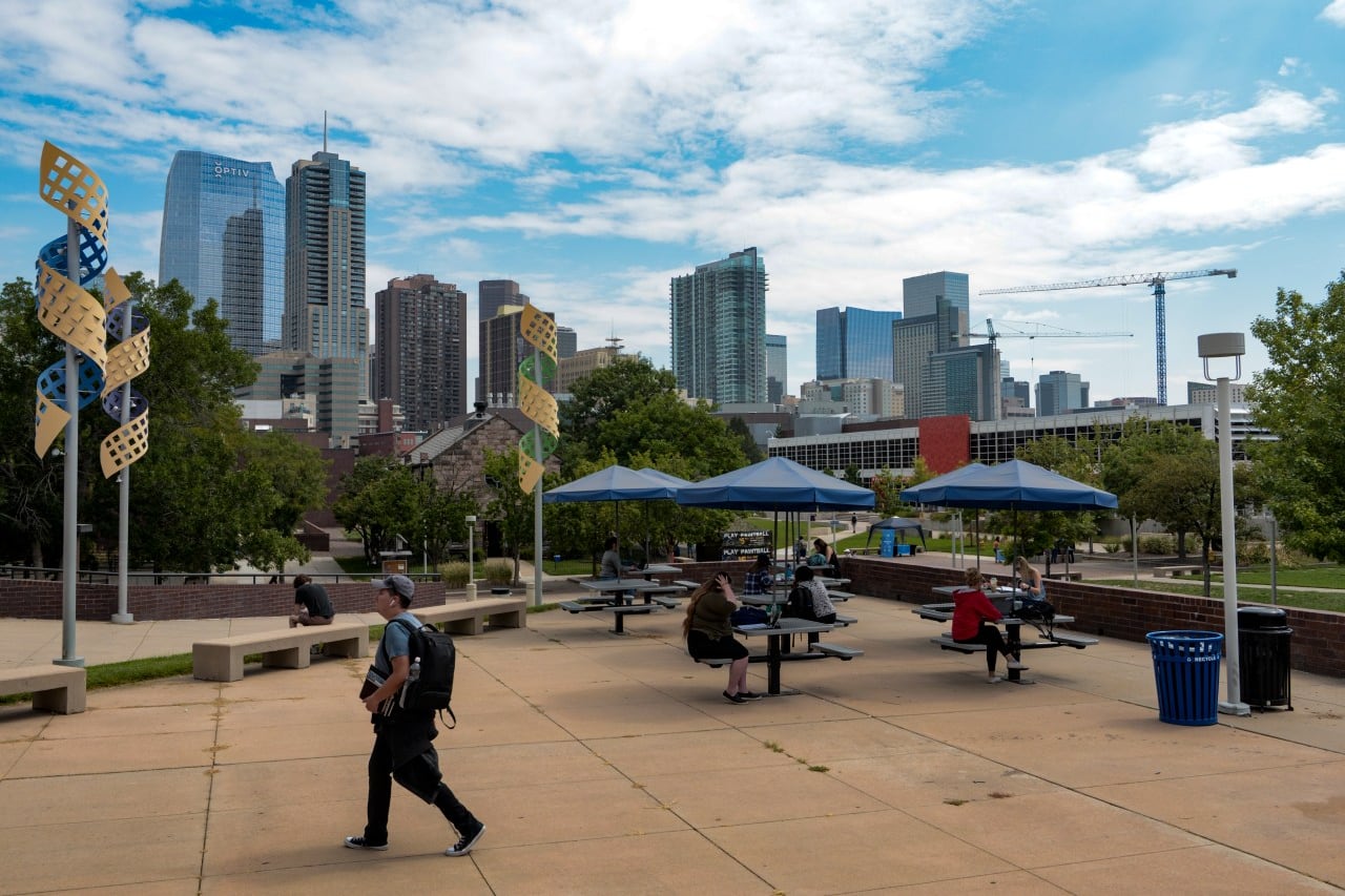 Students walk in a courtyard on a college campus with a skyline of skyscrapers in the background.