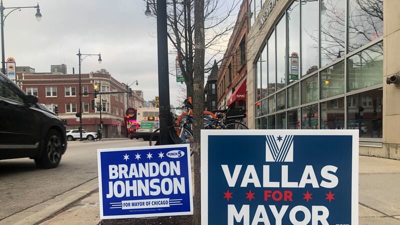 Two campaign yard signs. One for Brandon Johnson and one for Paul Vallas are posted along a Chicago sidewalk.