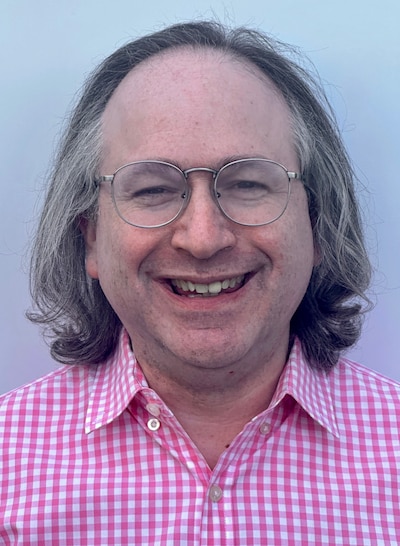 A portrait of a man in glasses with a pink-and-white checked shirt.