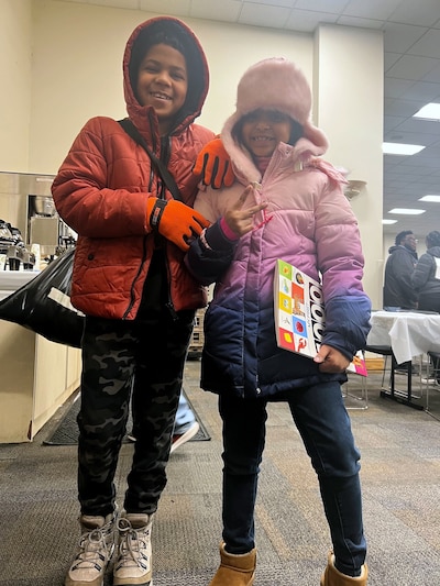 Two young children stand next to each other wearing coats smile for a photo.