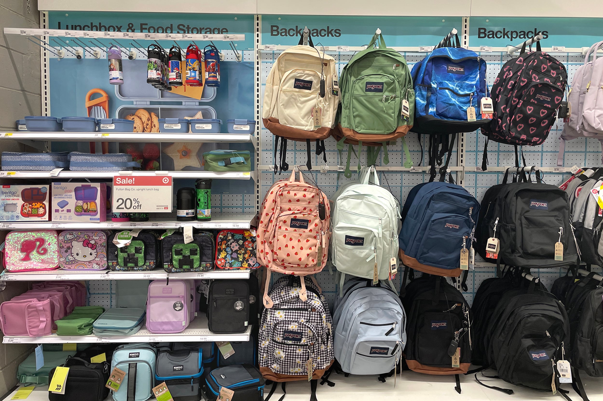 A photograph of a school display of lunchboxes and backpacks hanging on a wall in a mega store.