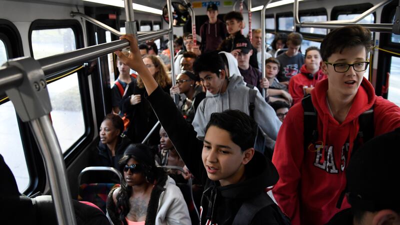 A city bus is packed with teenagers, many of them wearing hoodies, hanging from the hand rails.