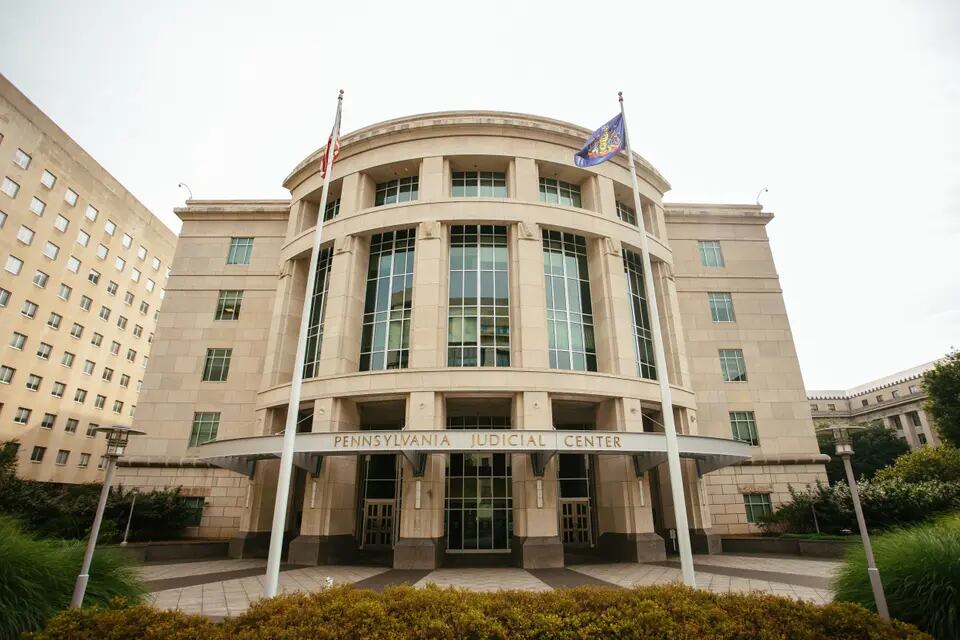 The front of a wide, stately tan building with a sign reading “Pennsylvania Judicial Center”