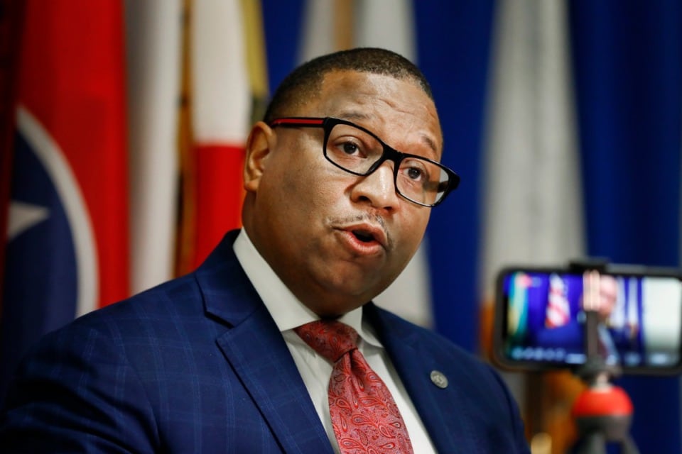 Man wearing a suit and glasses speaks in front of a camera