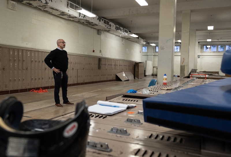 A man stands in a dilapidated school hallway.