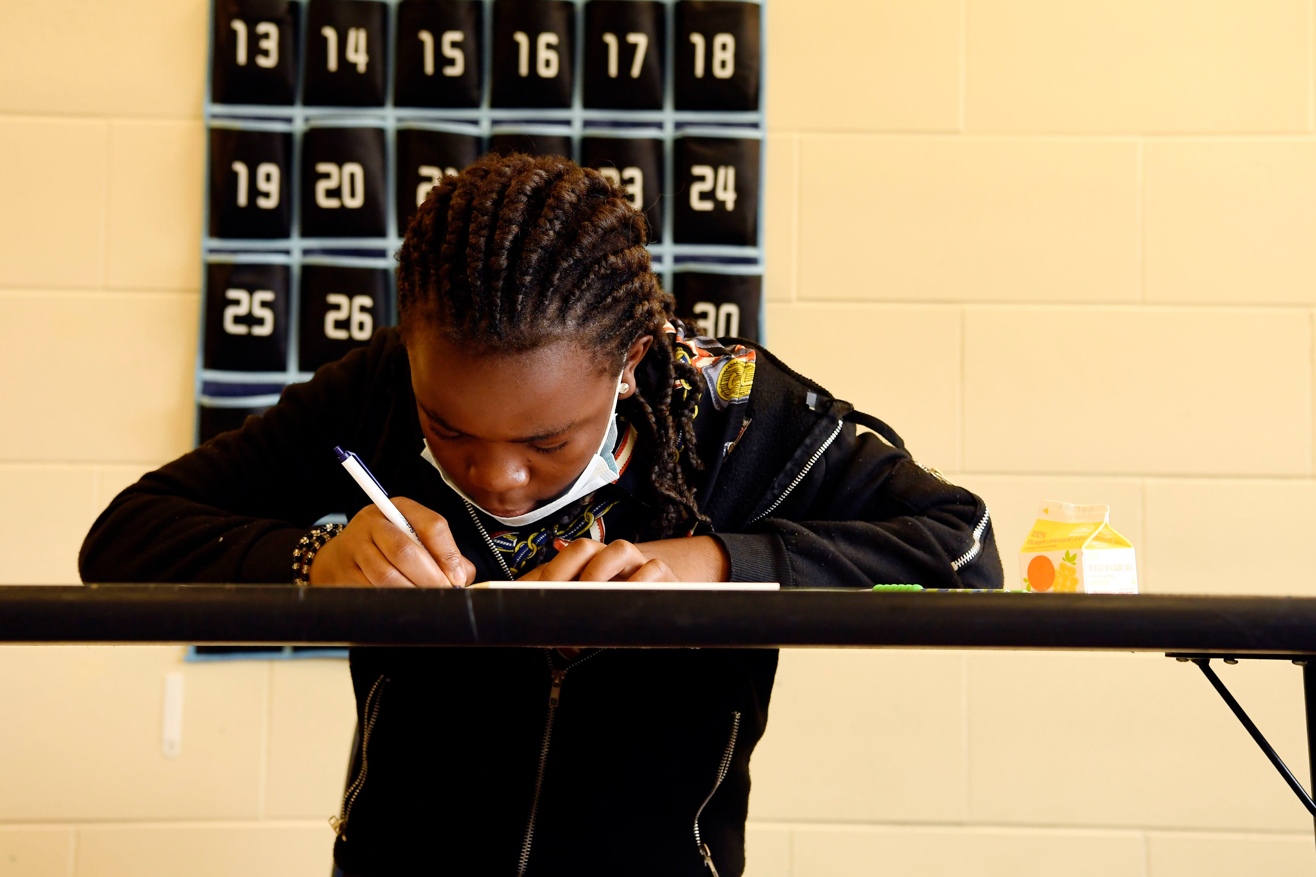 Student writing at a table in a classroom.