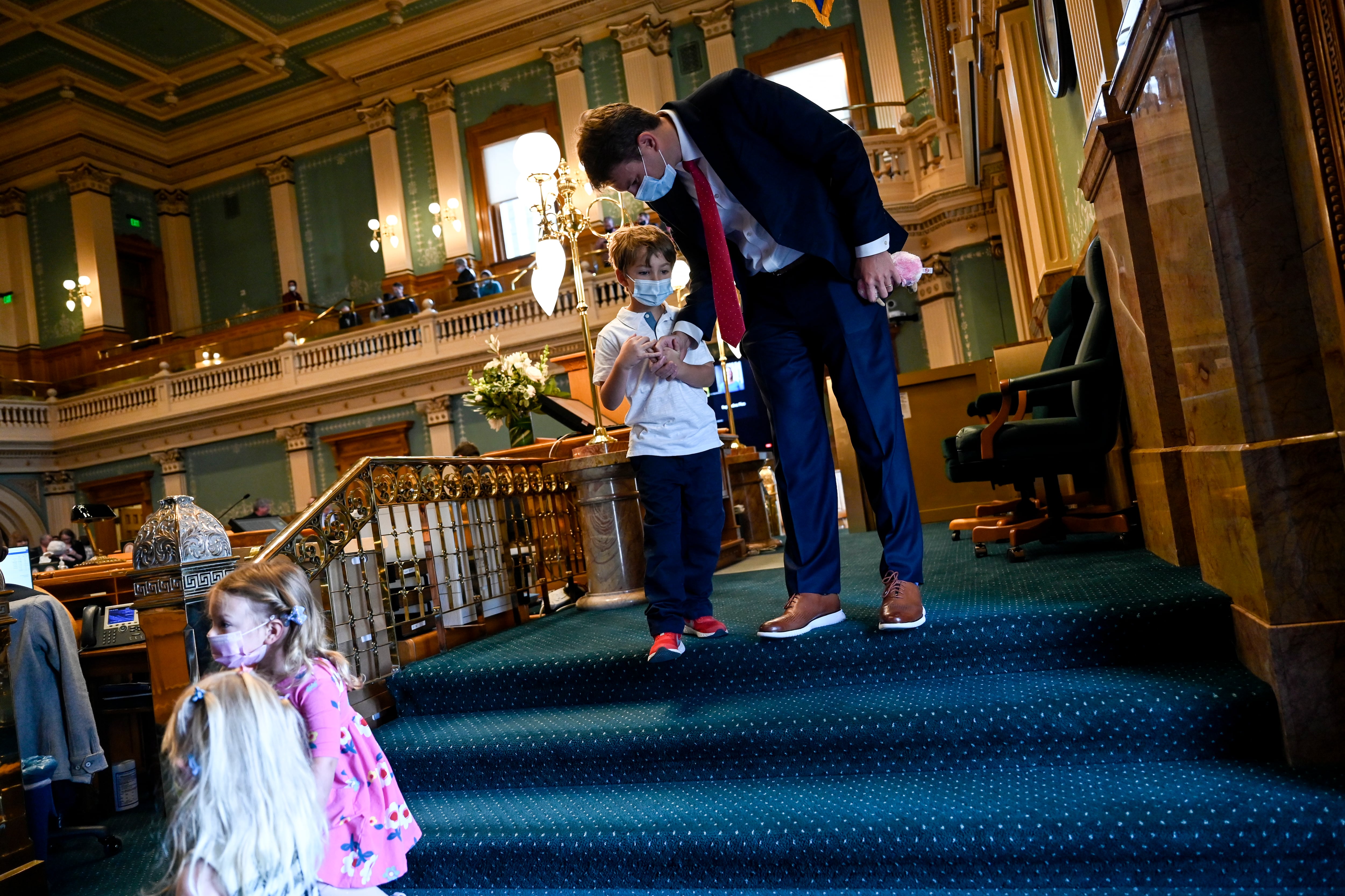 A man leans down to talk to his young son on the floor of the Colorado Statehouse