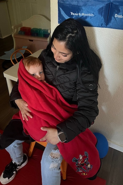 A photograph of a women with long dark hair holding a young child wrapped up in a red blanket.