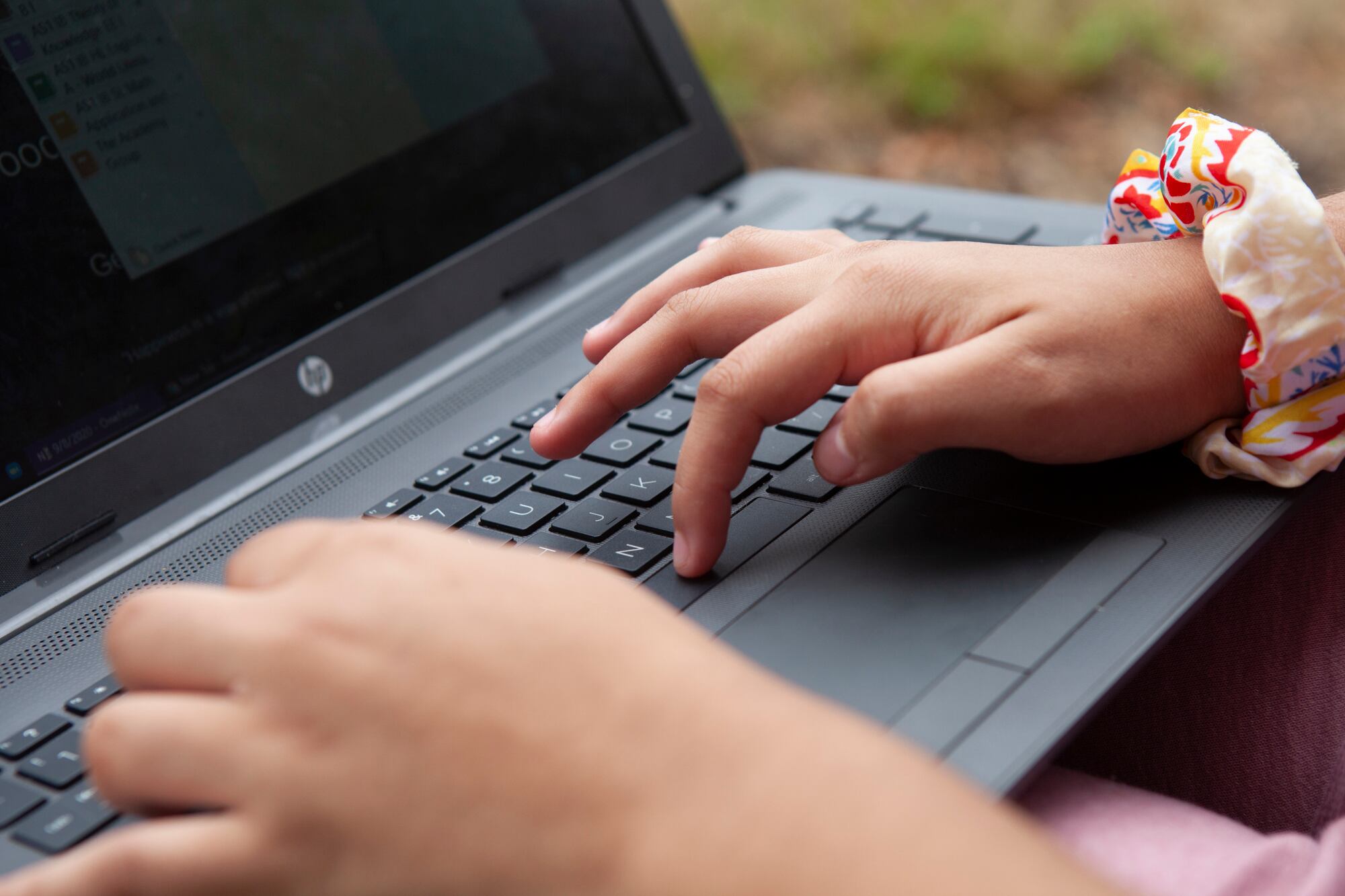 Close up of a student’s hands typing on a laptop with grass in the background.