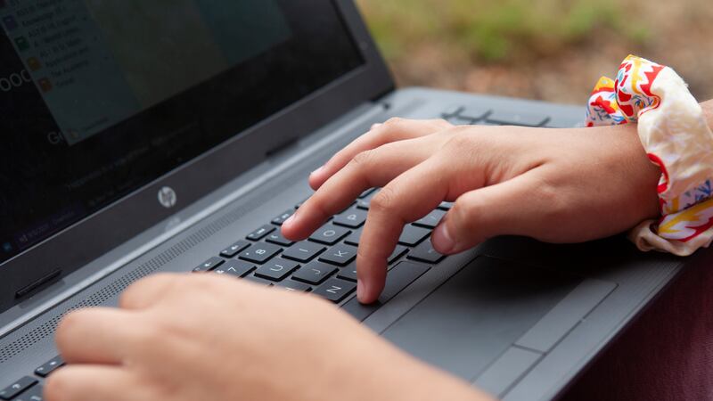 Close up of a student’s hands typing on a laptop with grass in the background.