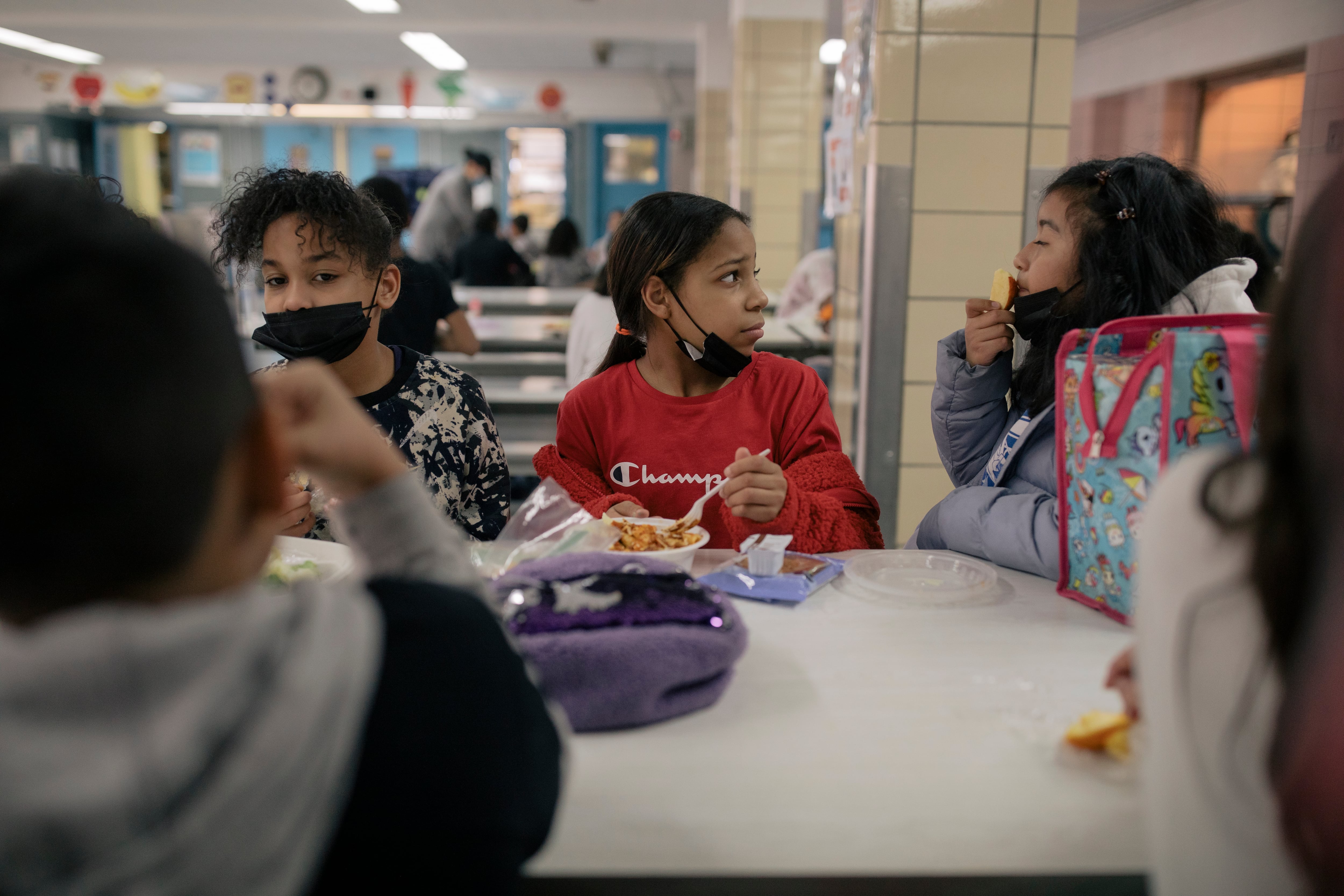 Three students in masks sit at a cafeteria table.