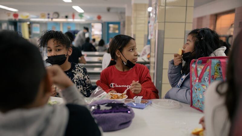 Three students in masks sit at a cafeteria table.