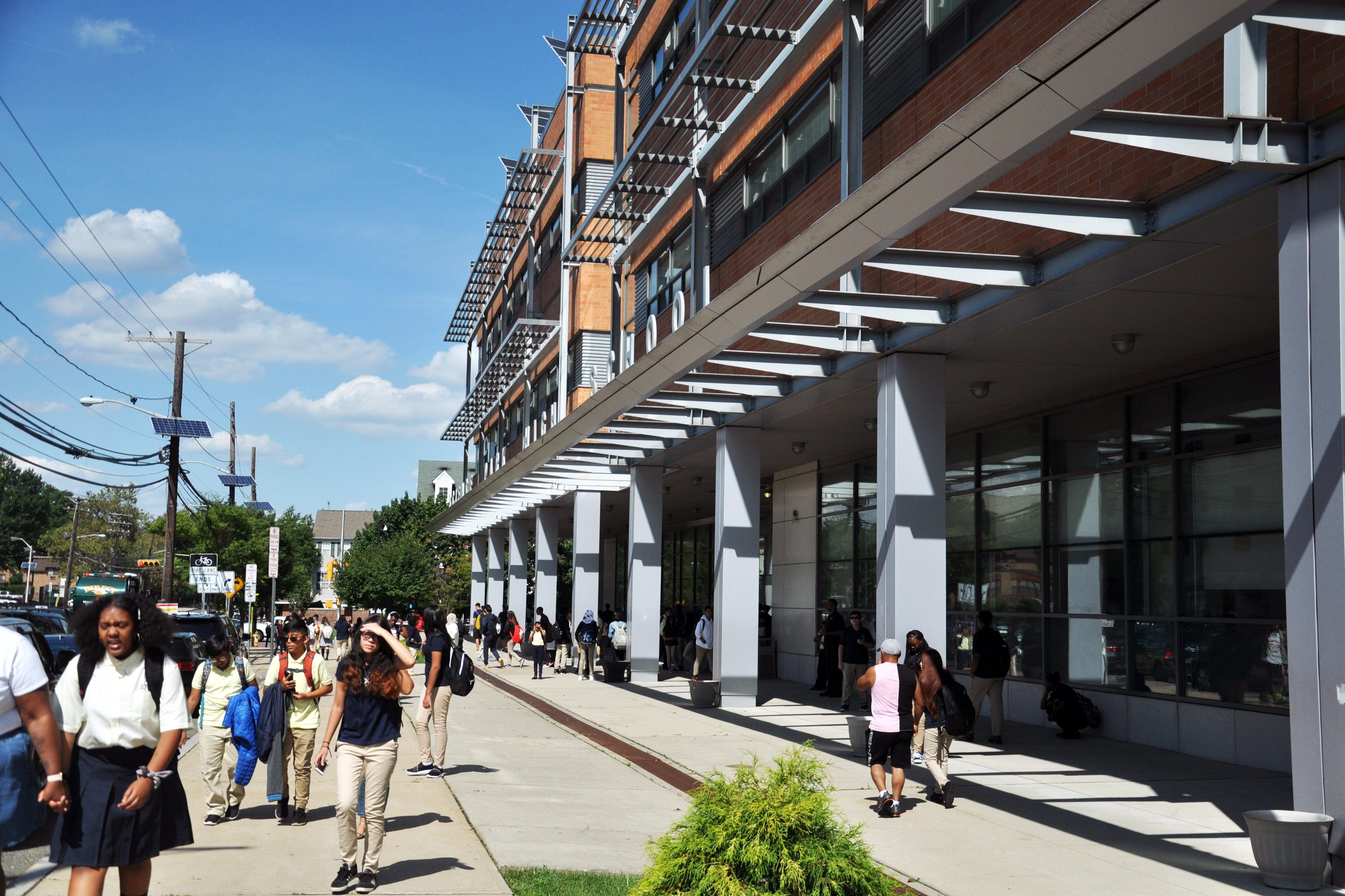 Students walk outside of a school on a sidewalk on a sunny day.
