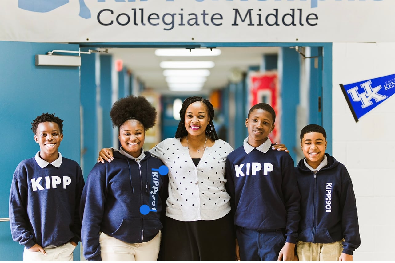 An educator stands in the middle of a school hallway flanked by four happy students.