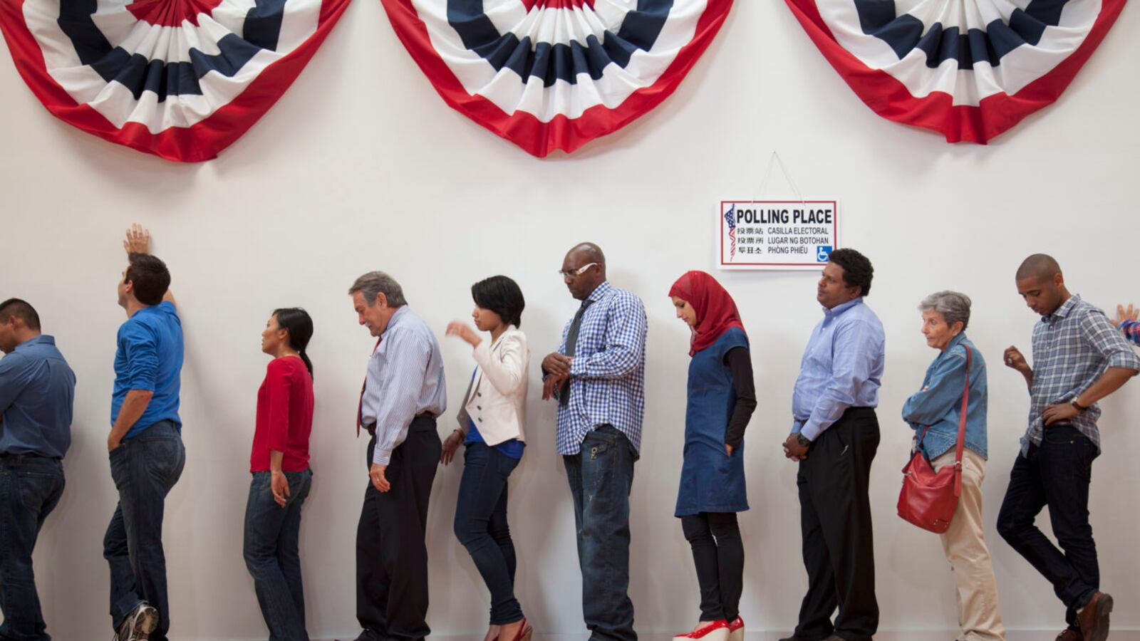People wait in line to vote at a polling station, with red, white, and blue banners hanging above them.