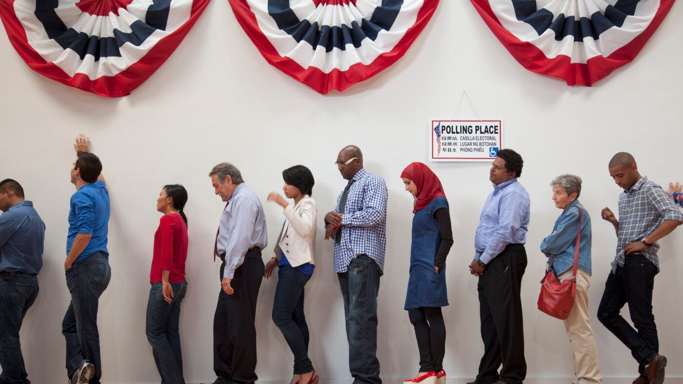 People wait in line to vote at a polling station, with red, white, and blue banners hanging above them.