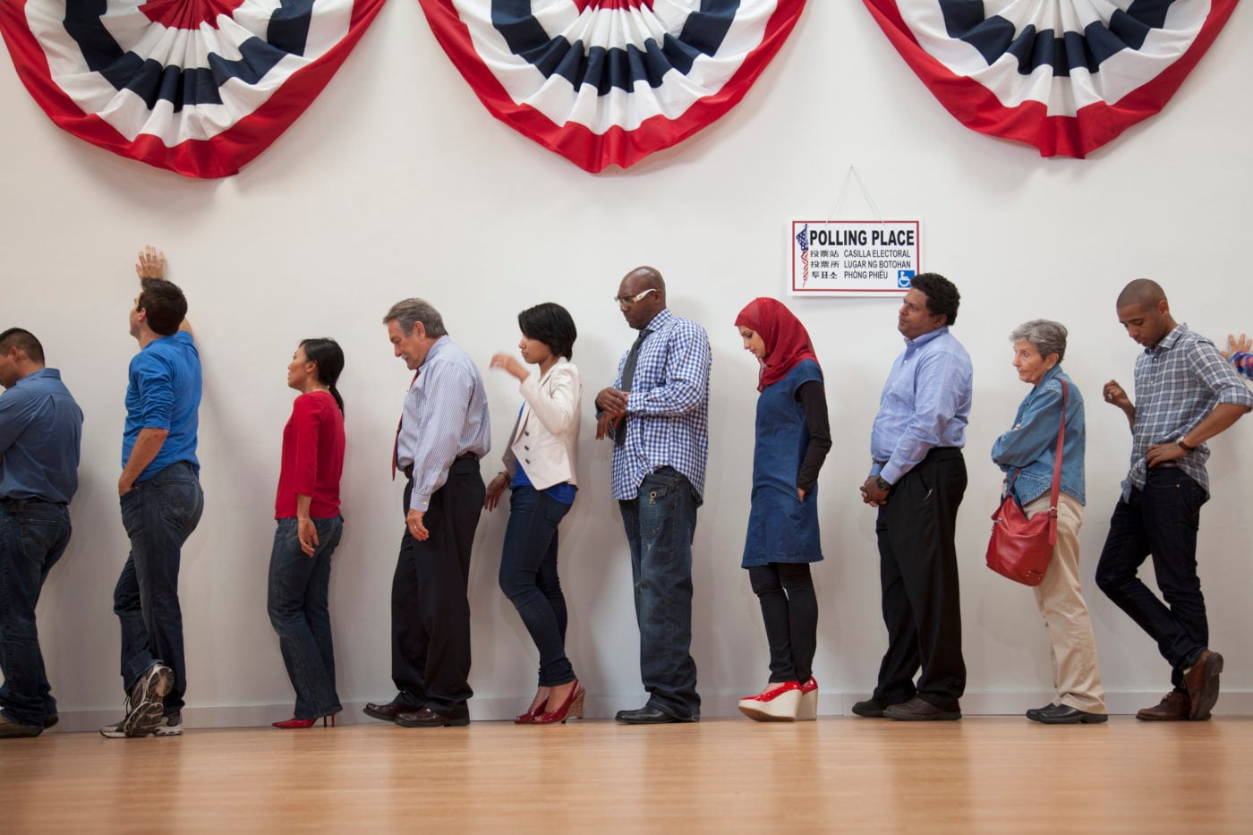 People wait in line to vote at a polling station, with red, white, and blue banners hanging above them.