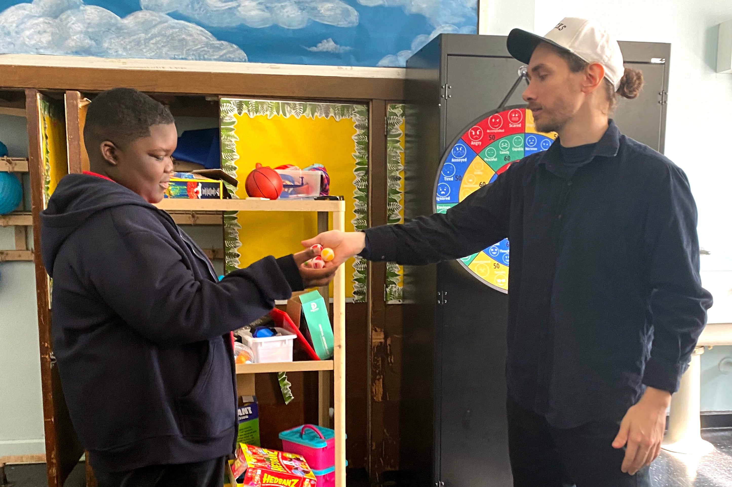 A man with a blue shirt hands something to a young man in a dark sweatshirt.
