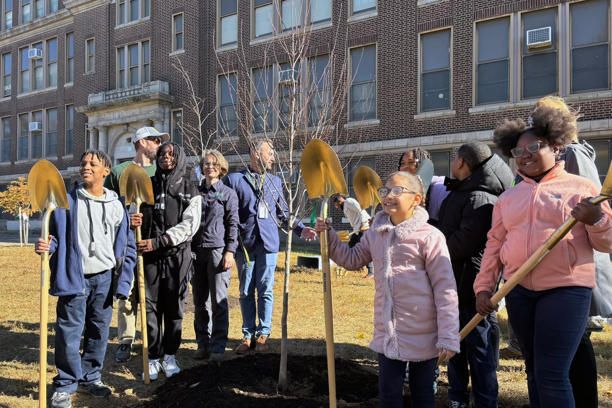 A group of students and adults stand outside with shovels.