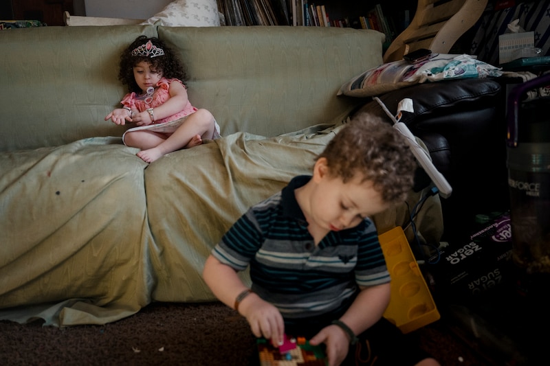 A photograph of a young girl sitting on a green couch while her older brother is sitting on the floor in the foreground.