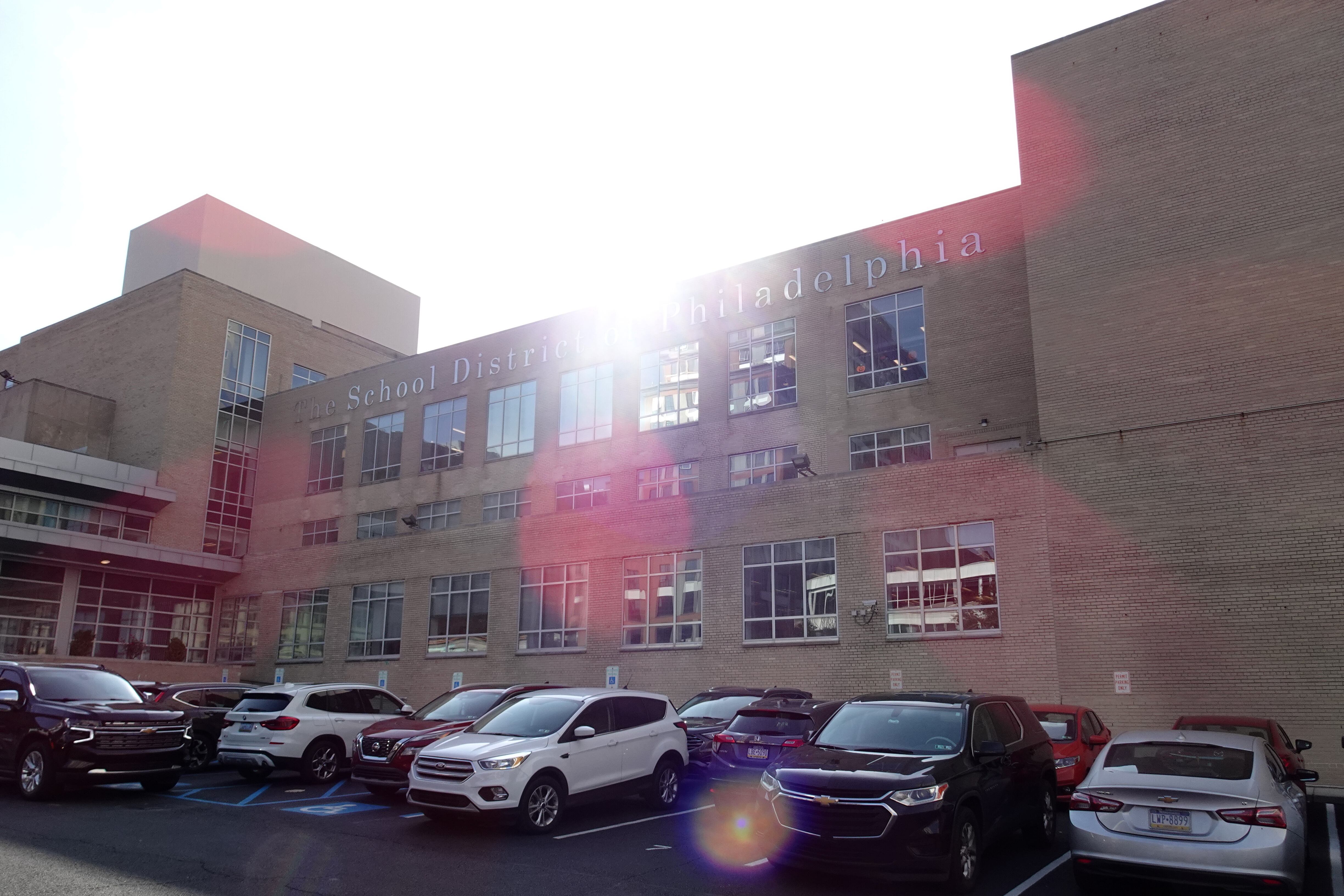 A large tan stone building with a row of parked cars out front.