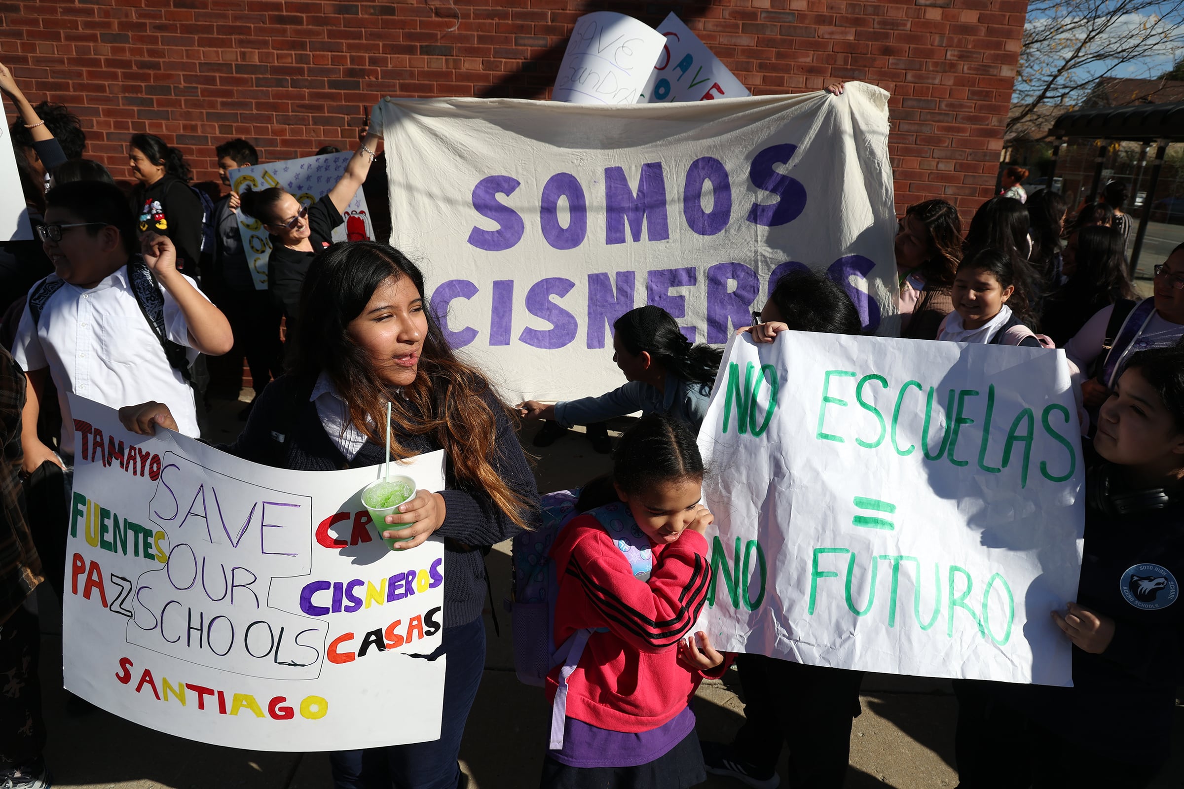 A group of people holds large signs outside on a sunny day during a protest.