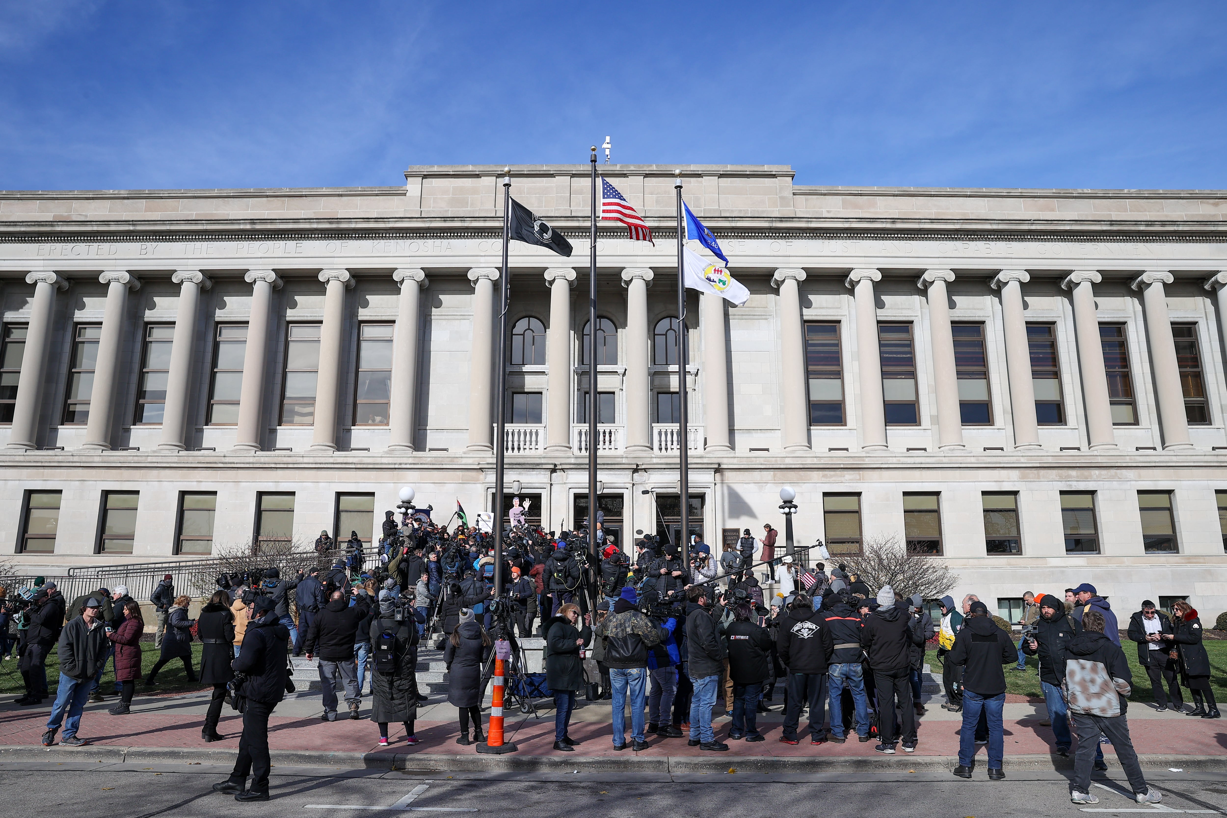 Several people gather on the steps of the Kenosha County Courthouse, a large building with rows of white pillars.