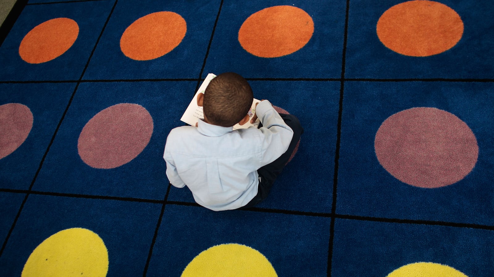 A student reads on a dotted carpet where students often sit for class at Harlem Success Academy.