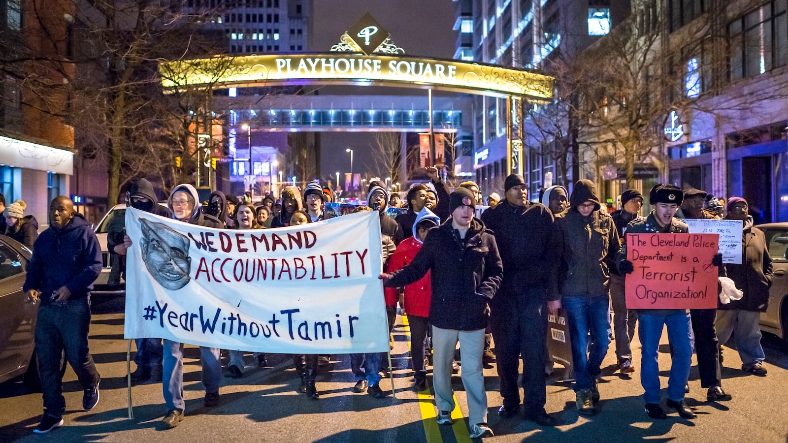 A group of protesters march downtown with a sign that reads, “We demand accountability. #YearWithoutTamir.”